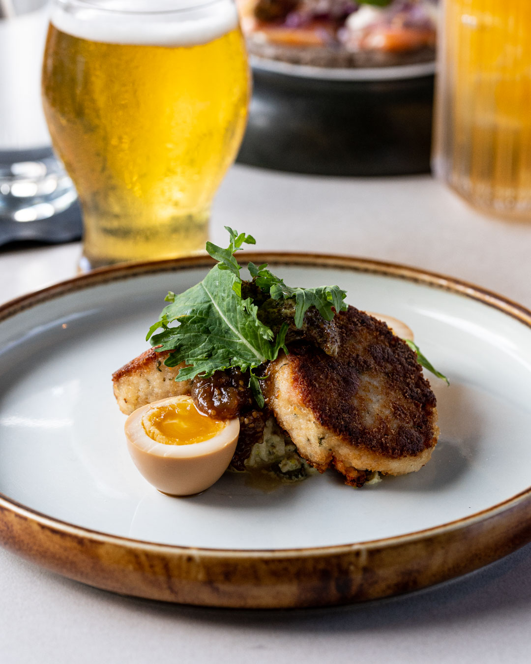 Haddock fish cakes with poached eggs, chow chow, spinach, kale, mustard sauce in white dish with brown trim